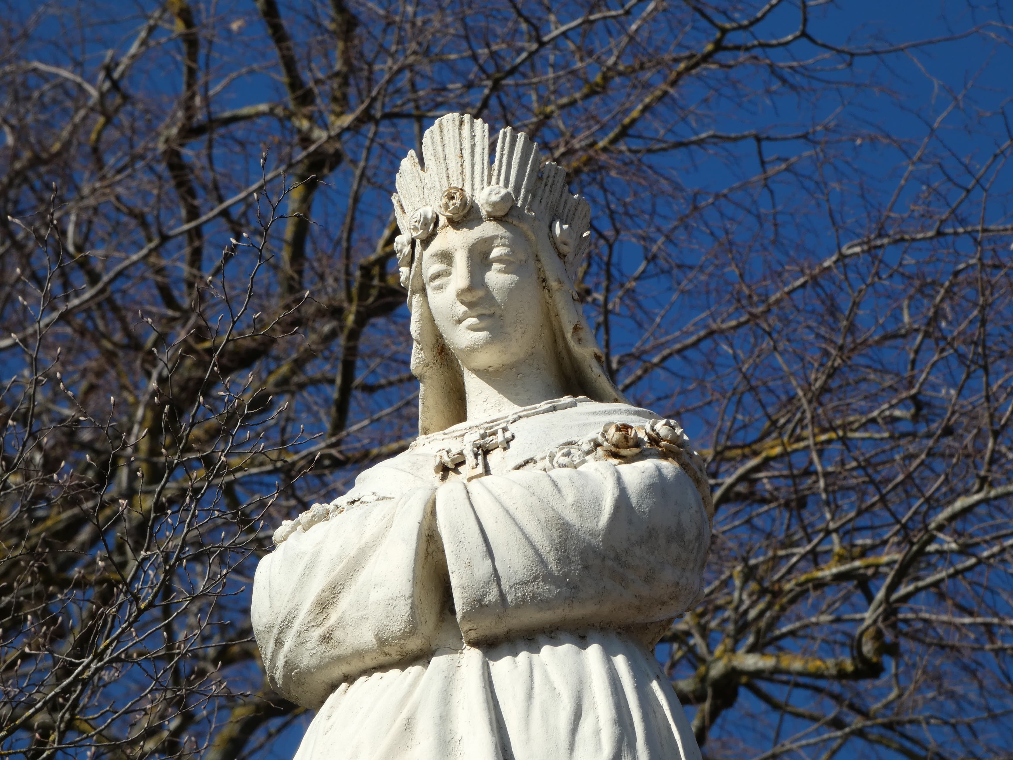 Kamienna figura Matki Bożej z La Salette w koronie z róż, z łańcuchem na ramionach i krzyżem na piersi